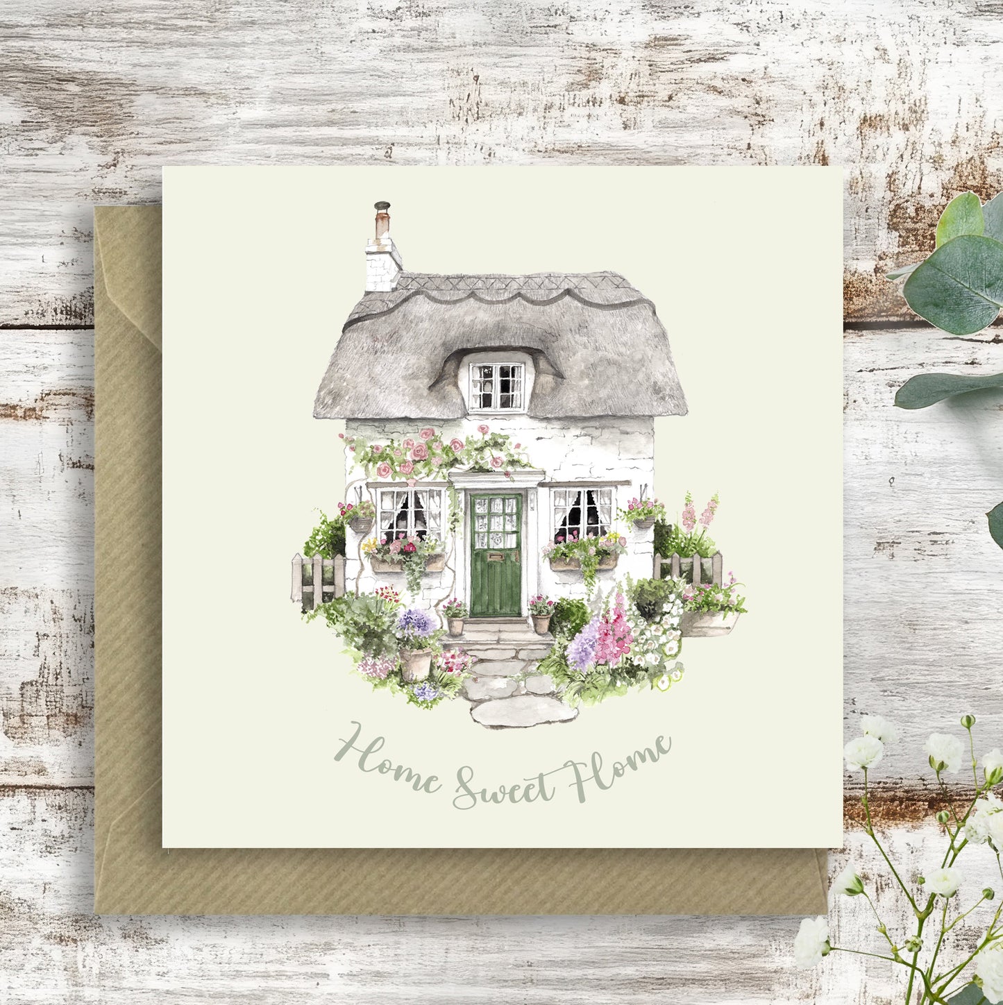 Greeting card with a thatched cottage illustration and 'Home Sweet Home' text on a wooden surface.