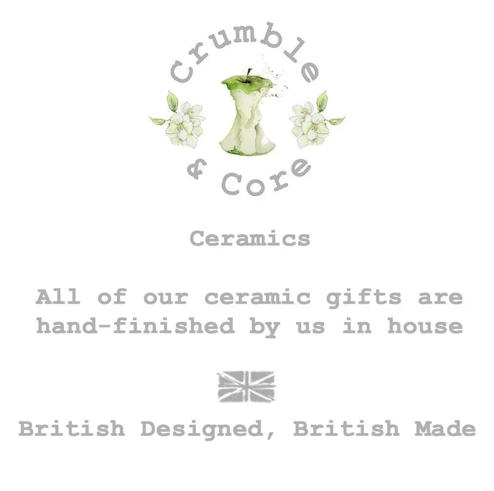 The image is a logo for a company called Crumble & Core, which specializes in ceramics. The logo features an apple with a green stem and leaves, surrounded by white flowers. The company's slogan, "All of our ceramic gifts are hand-finished by us in house", is displayed below the logo. The company's British-designed, British-made tagline is also included in the image.